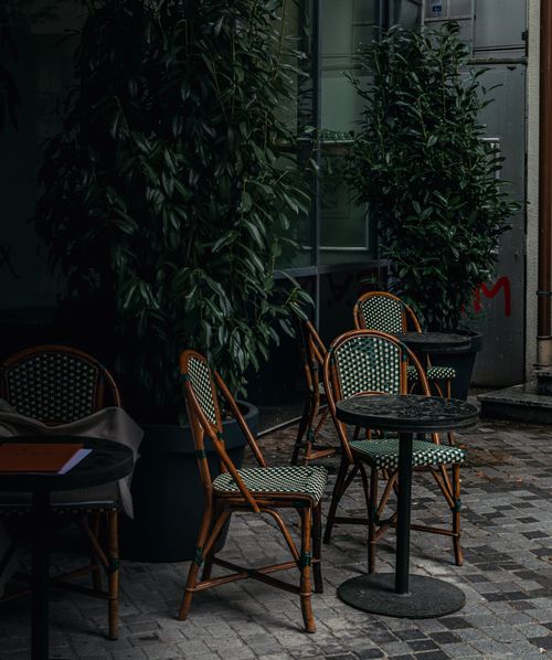 Free A charming outdoor café patio with empty seats and lush plants, creating a cozy ambiance. Stock Photo