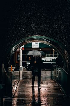 A man walks with an umbrella through a dimly lit, rainy city street at night.