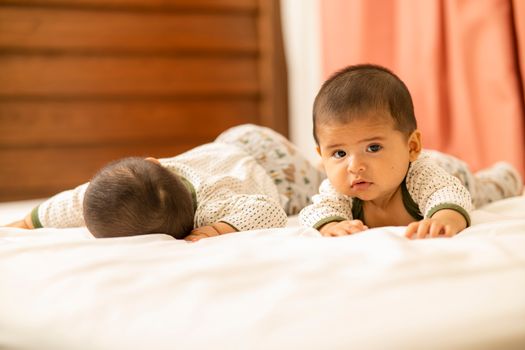 Cute twin babies with short hair lying on a bed, creating a heartwarming scene.