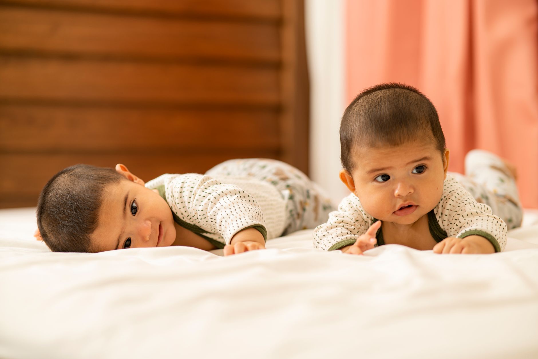 Adorable twin babies lying on a bed indoors, showcasing sibling love and bonding in a cozy setting.