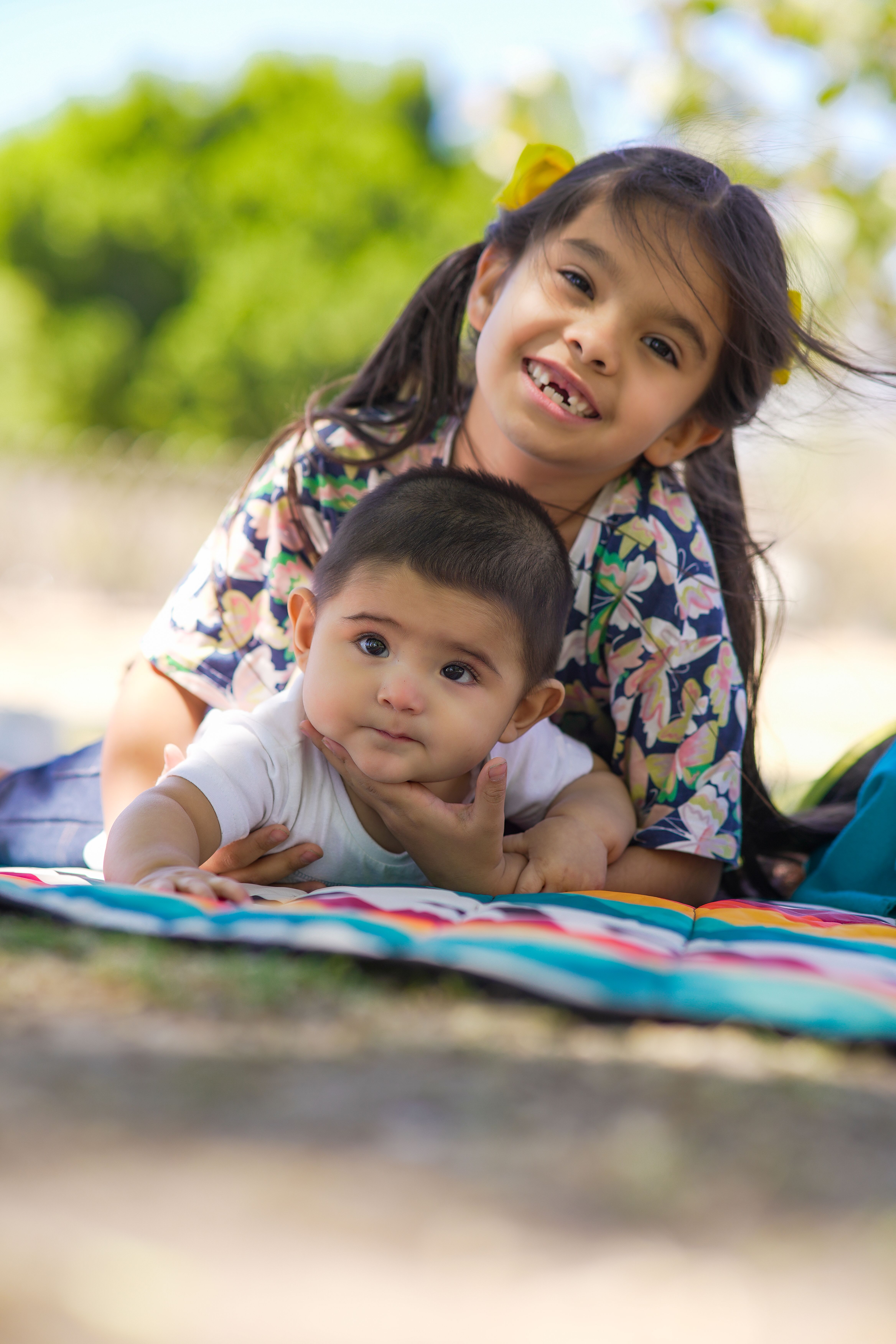 Fotomural Hermana y hermano sonriendo en una manta colorida al aire libre en un día soleado.