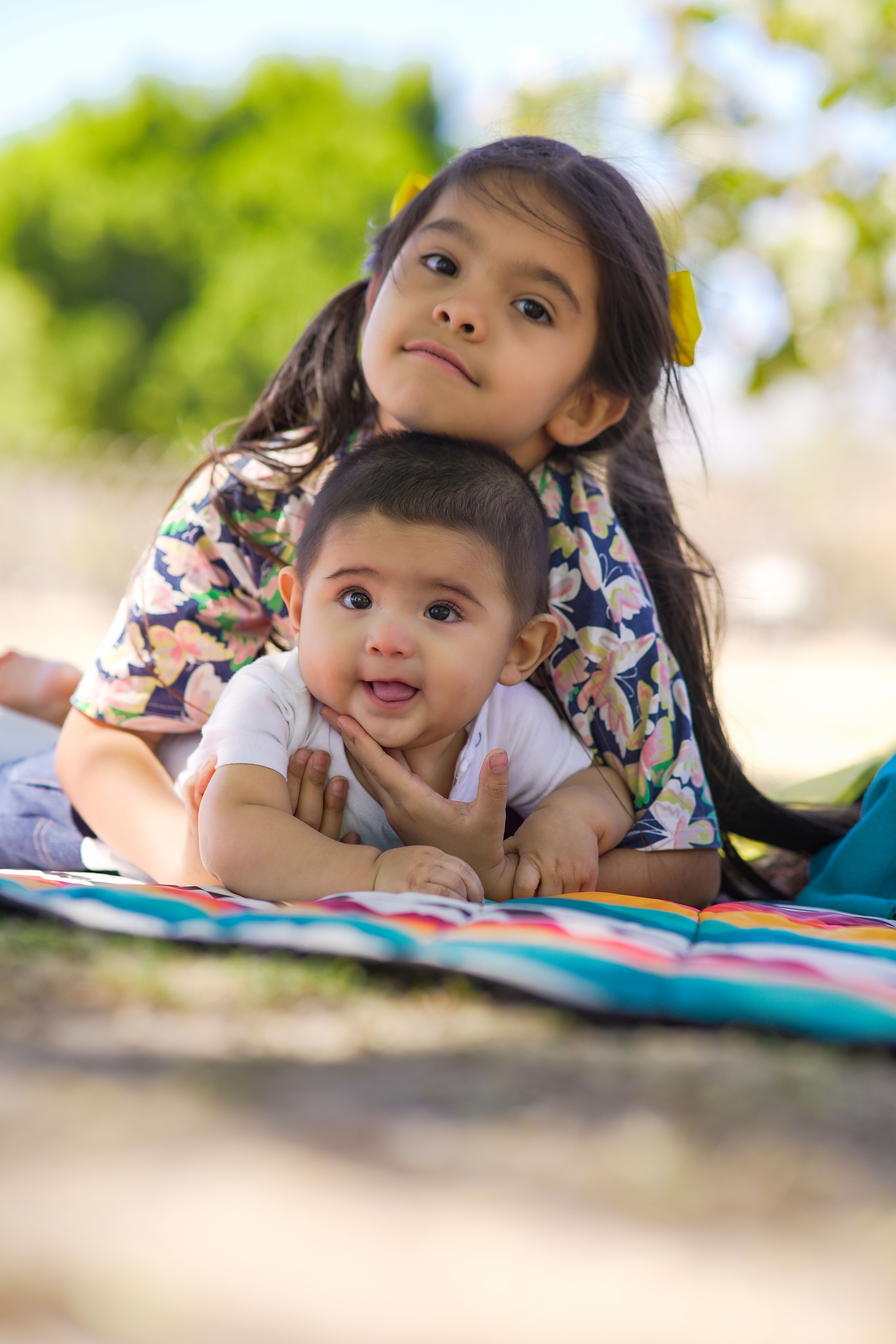 Fotomural Una niña y su hermanito disfrutan de un día soleado al aire libre, tumbados sobre una manta colorida.