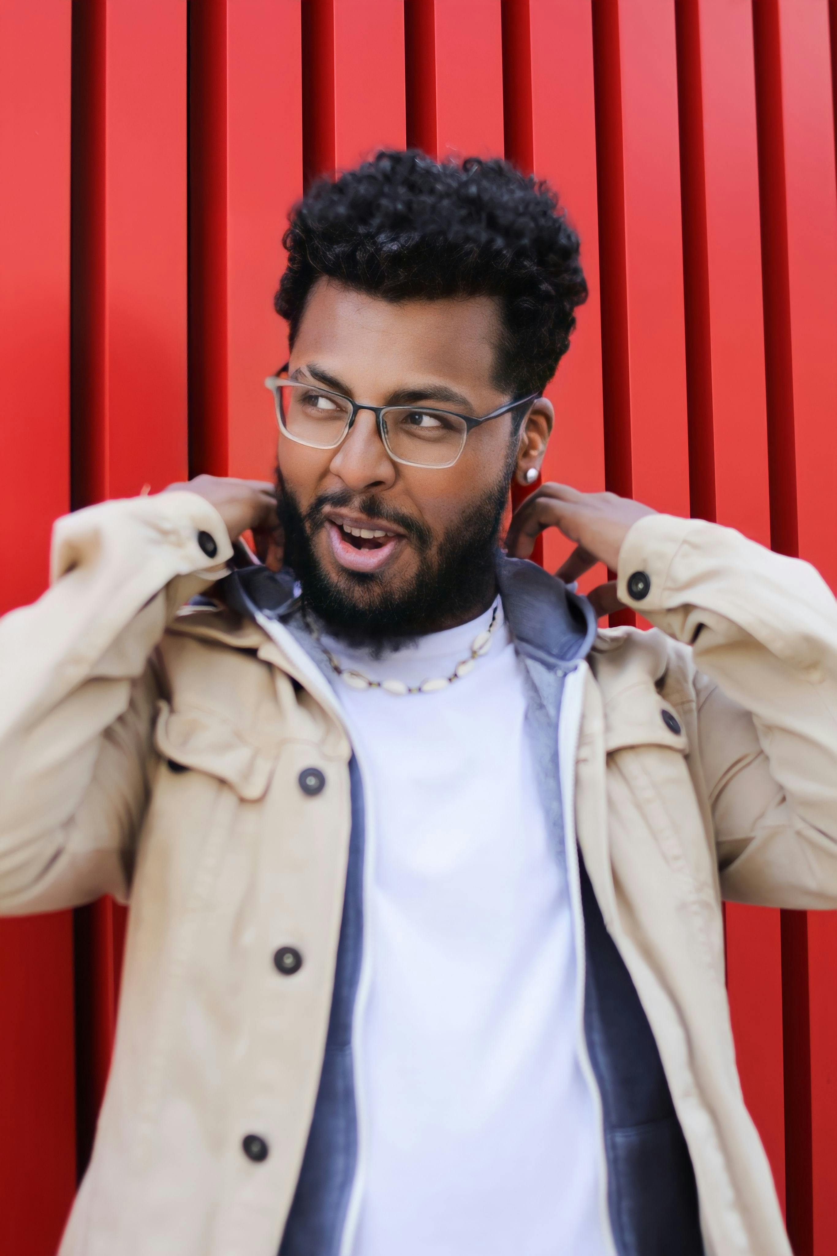 Stylish man with beard and glasses posing against vibrant red backdrop.