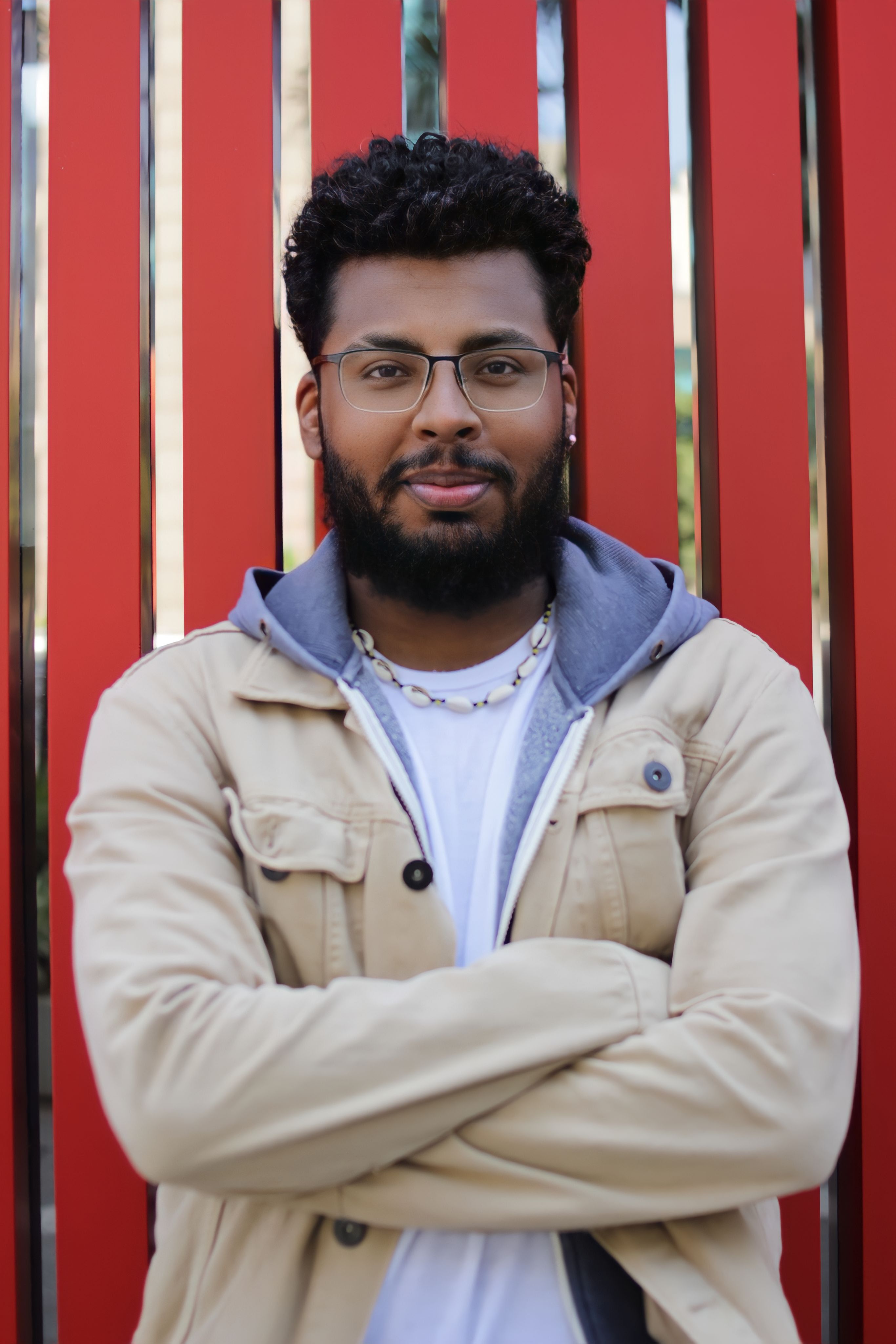 Stylish man with eyeglasses stands confidently against a vibrant red background.