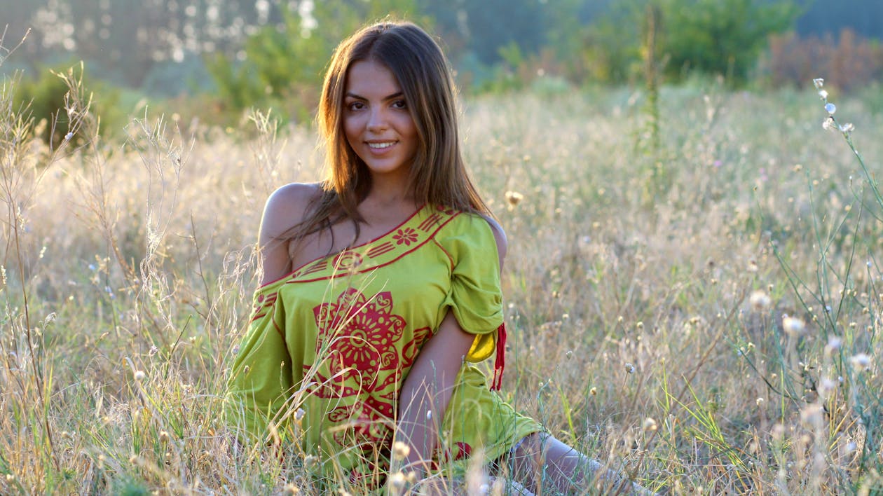 Free Woman Wearing Yellow and Red Dress Sitting on the Ground While Looking at the Camera Stock Photo