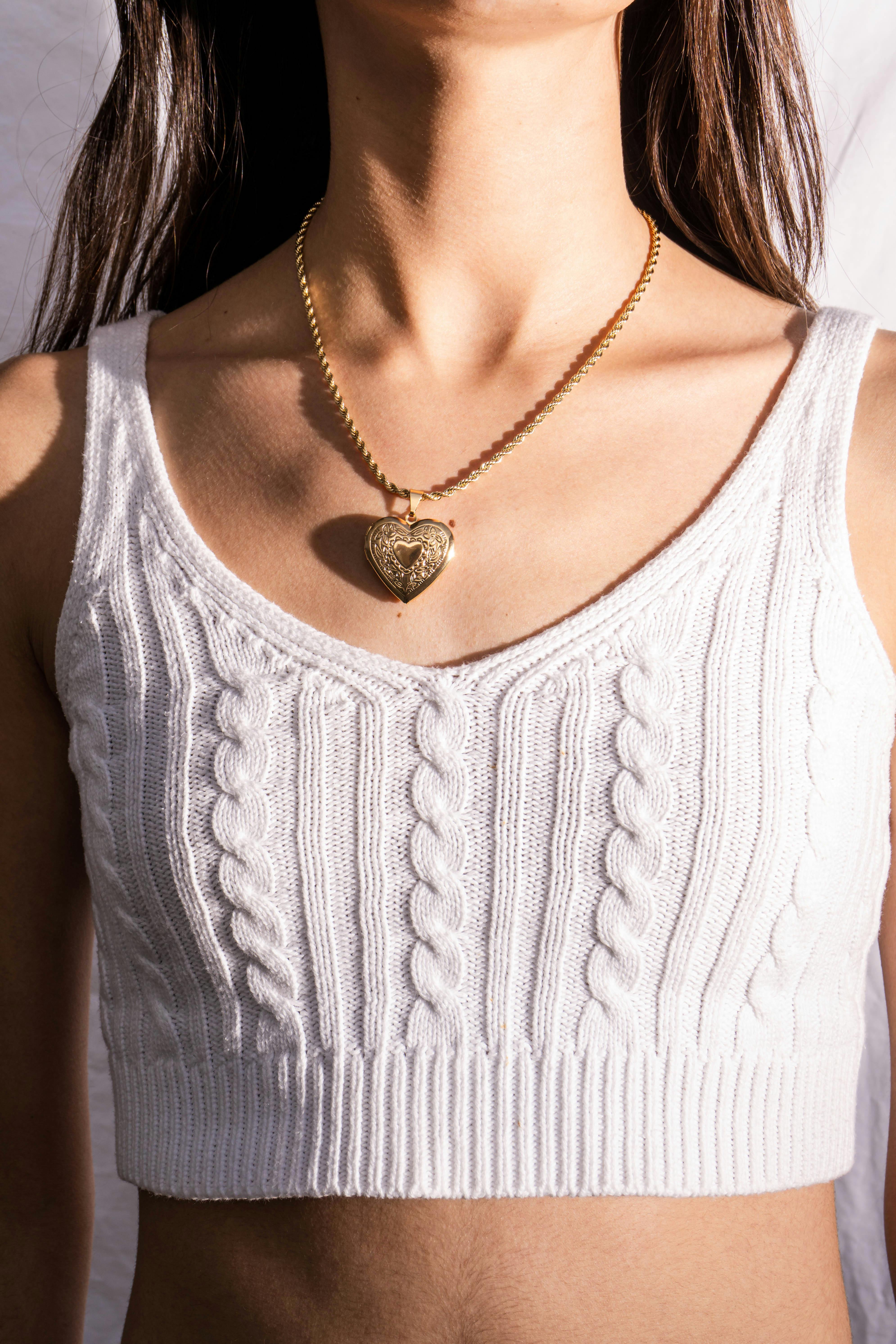 Free Close-up of a woman wearing a knitted tank top with a heart-shaped pendant necklace. Stock Photo