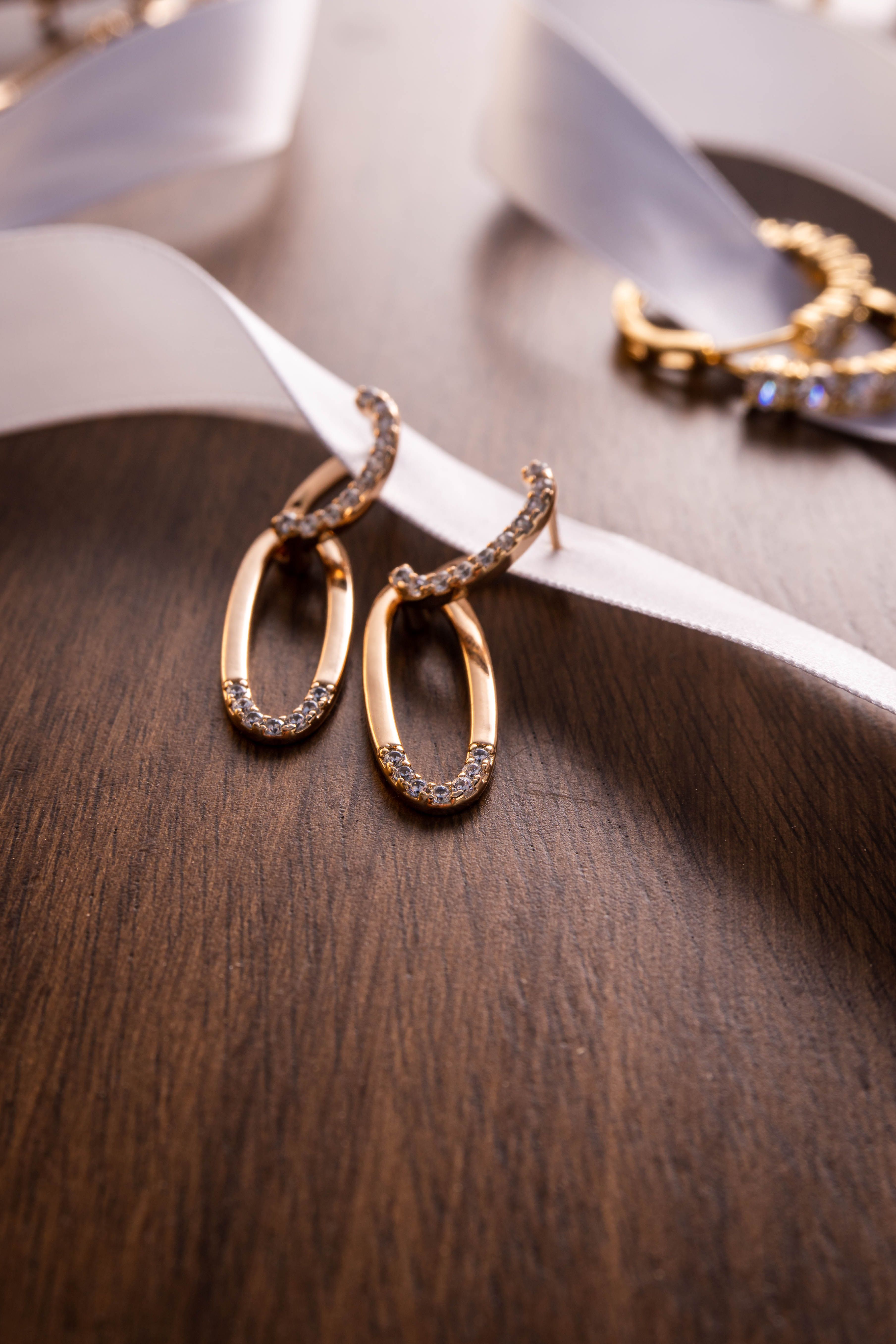 Close-up of gold hoop earrings with diamonds on wood and ribbon background.