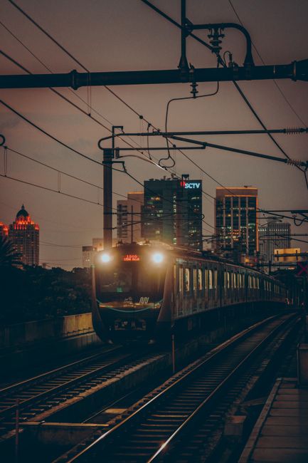 Evening scene of a train approaching a station in urban Jakarta featuring skyscrapers.