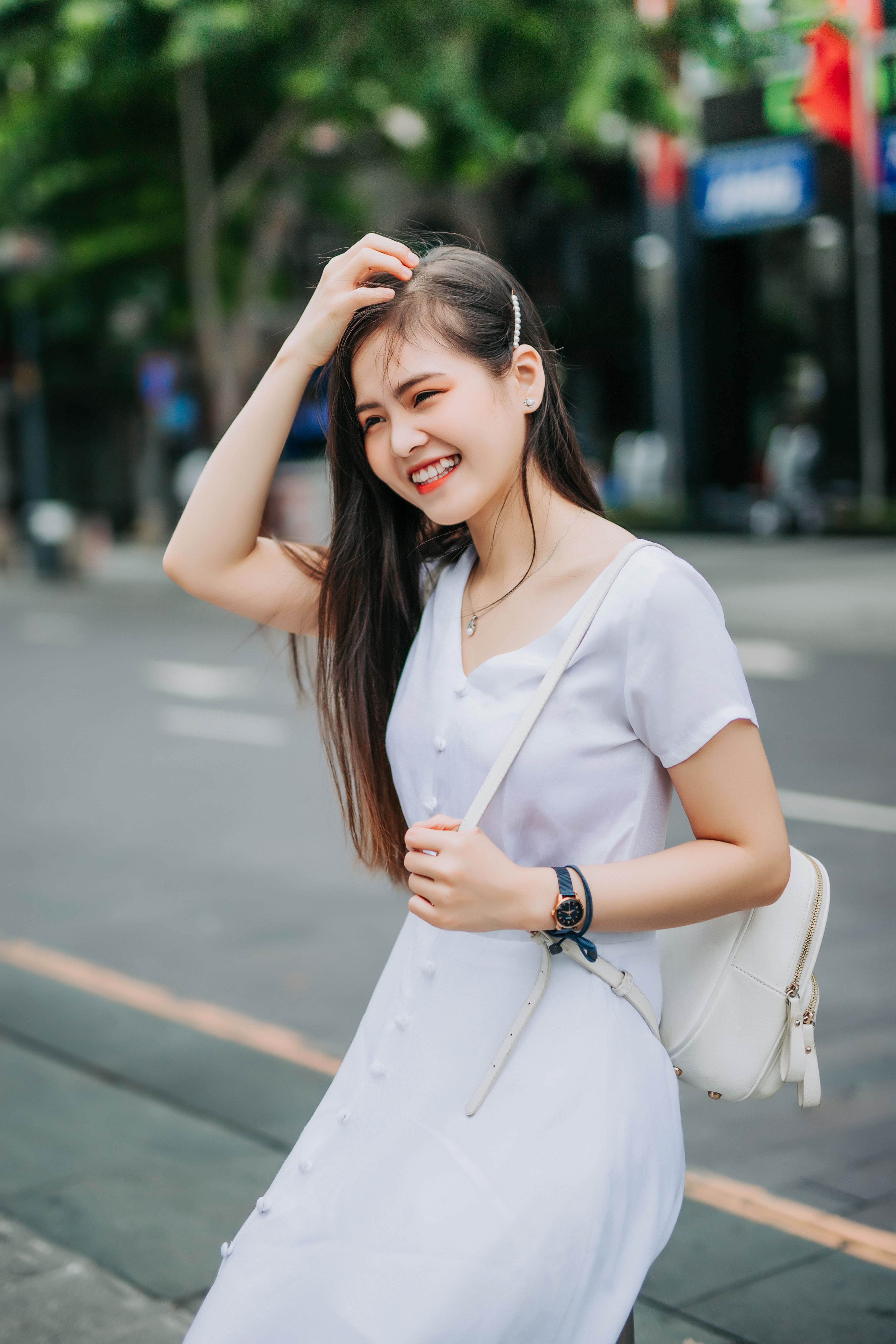 A smiling woman in a white dress enjoys a sunny day on Ho Chi Minh City street.