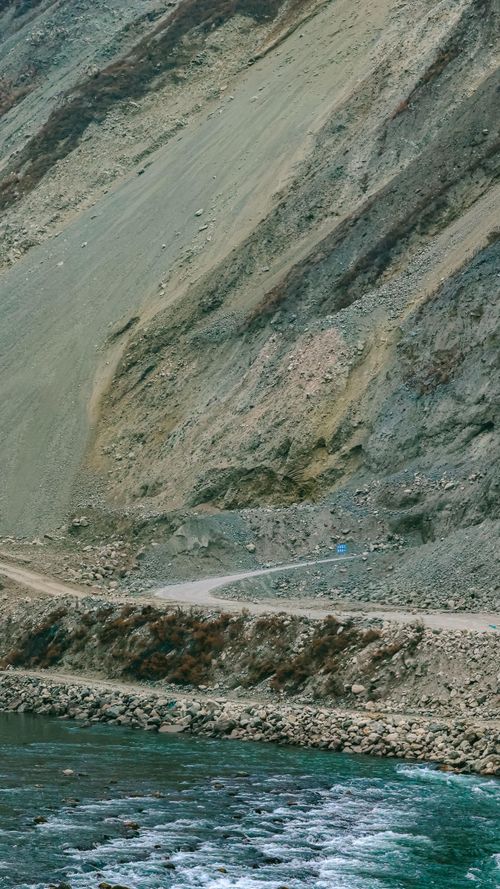 Free Aerial view of a winding road alongside a river at the base of a rugged mountain slope. Stock Photo