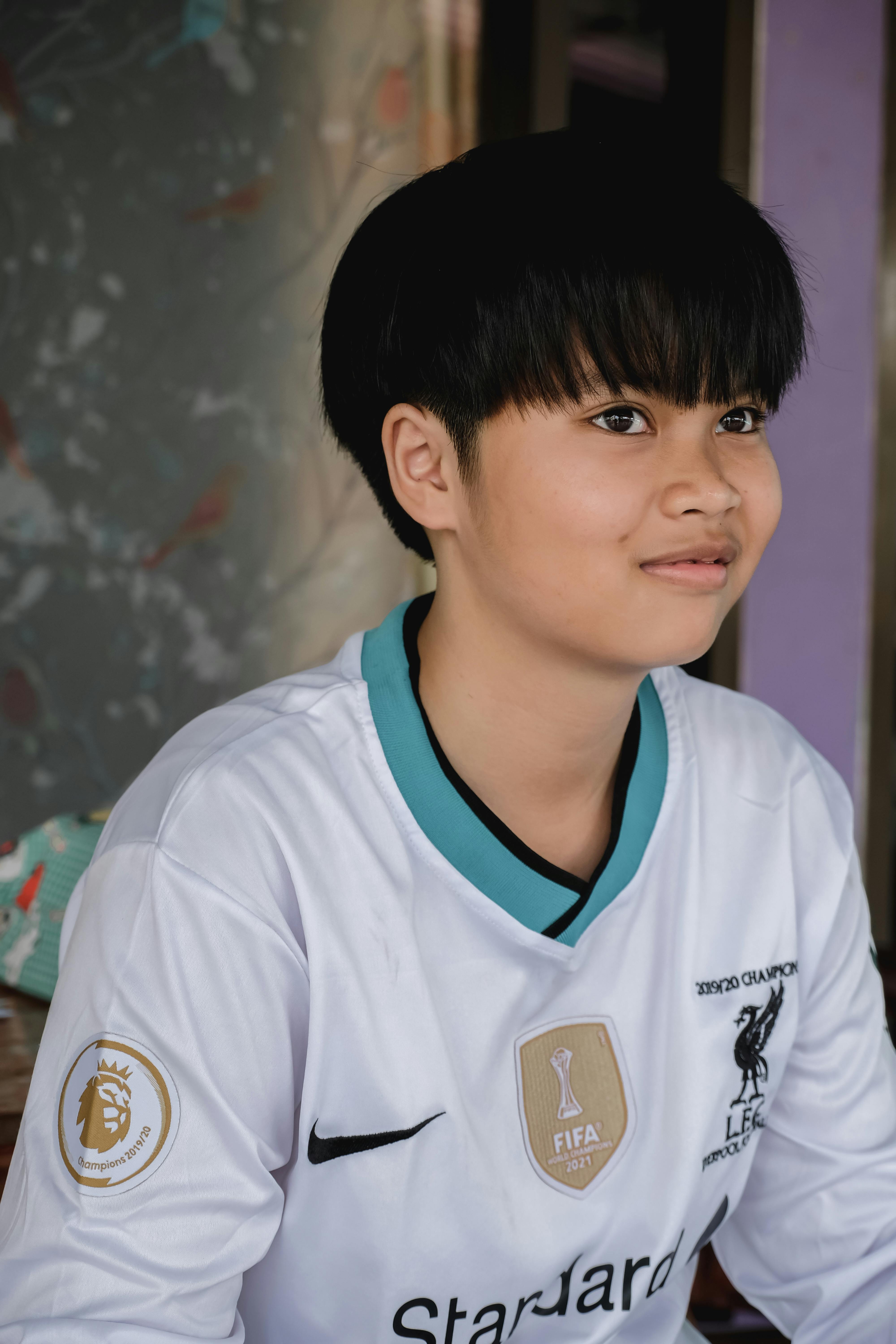 A young soccer fan in a team jersey smiles enthusiastically indoors.