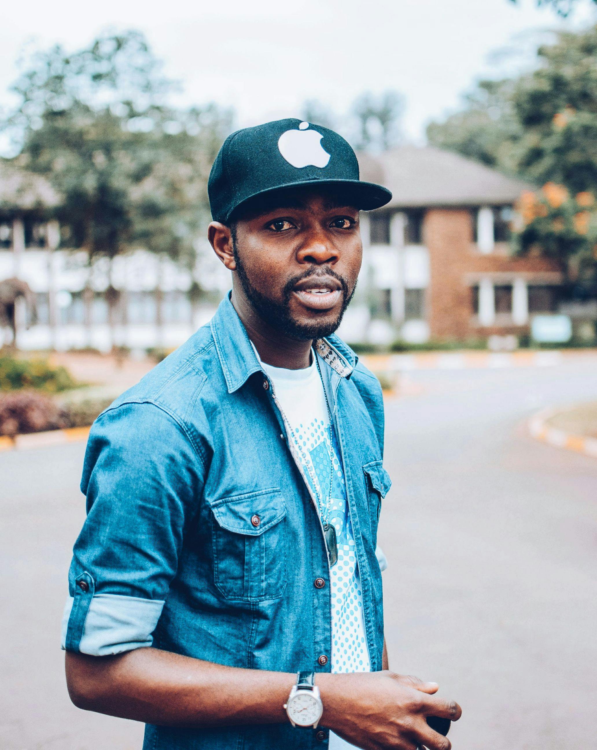 一位穿着牛仔布衣、戴着帽子的非裔美国人在户外摆出休闲的姿势