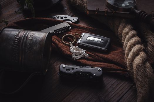 A vintage-themed still life featuring a keychain, rope, knife, and an engraved mug on a wooden table.