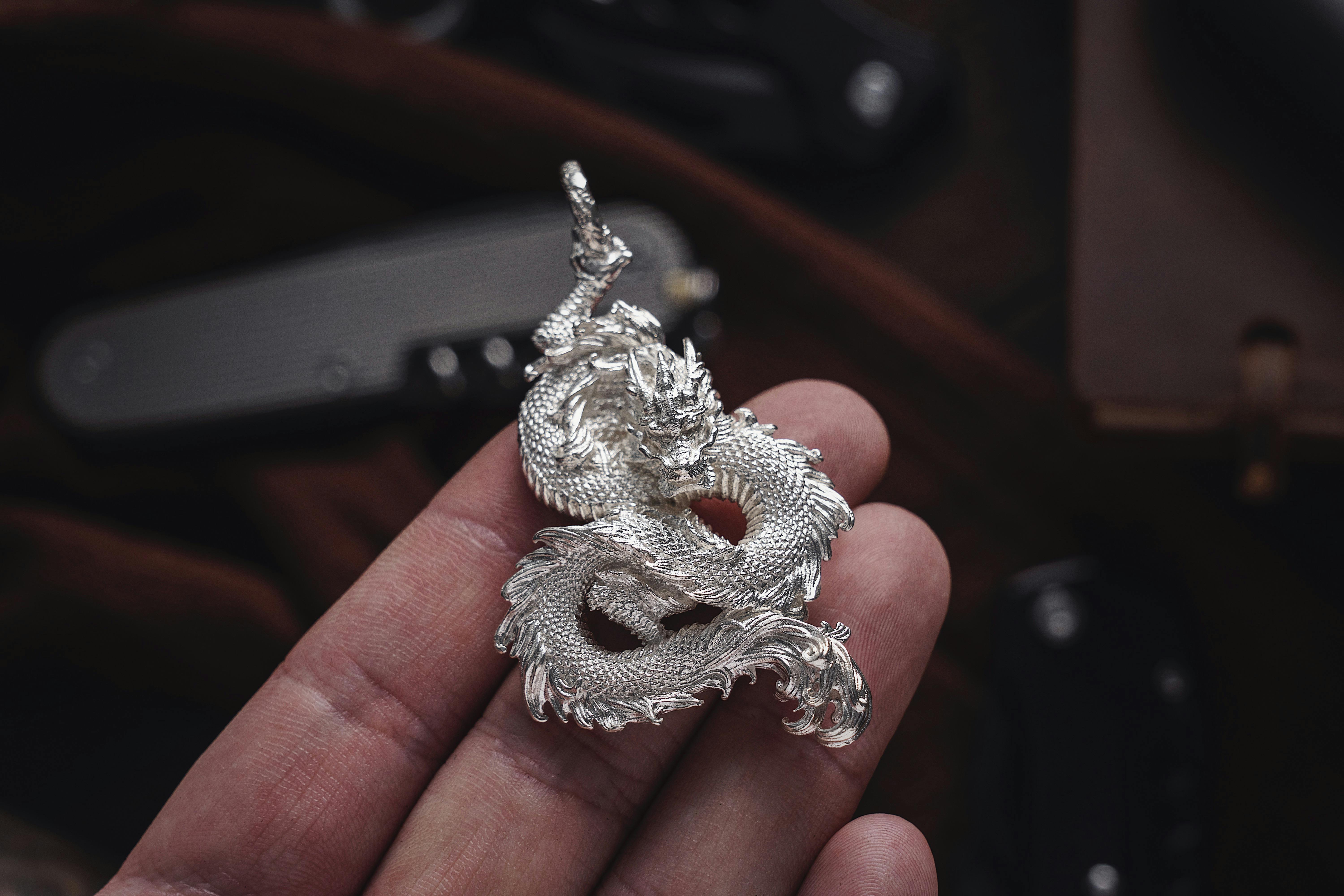 A close-up of a silver dragon figurine held in a hand, showcasing exquisite craftsmanship.