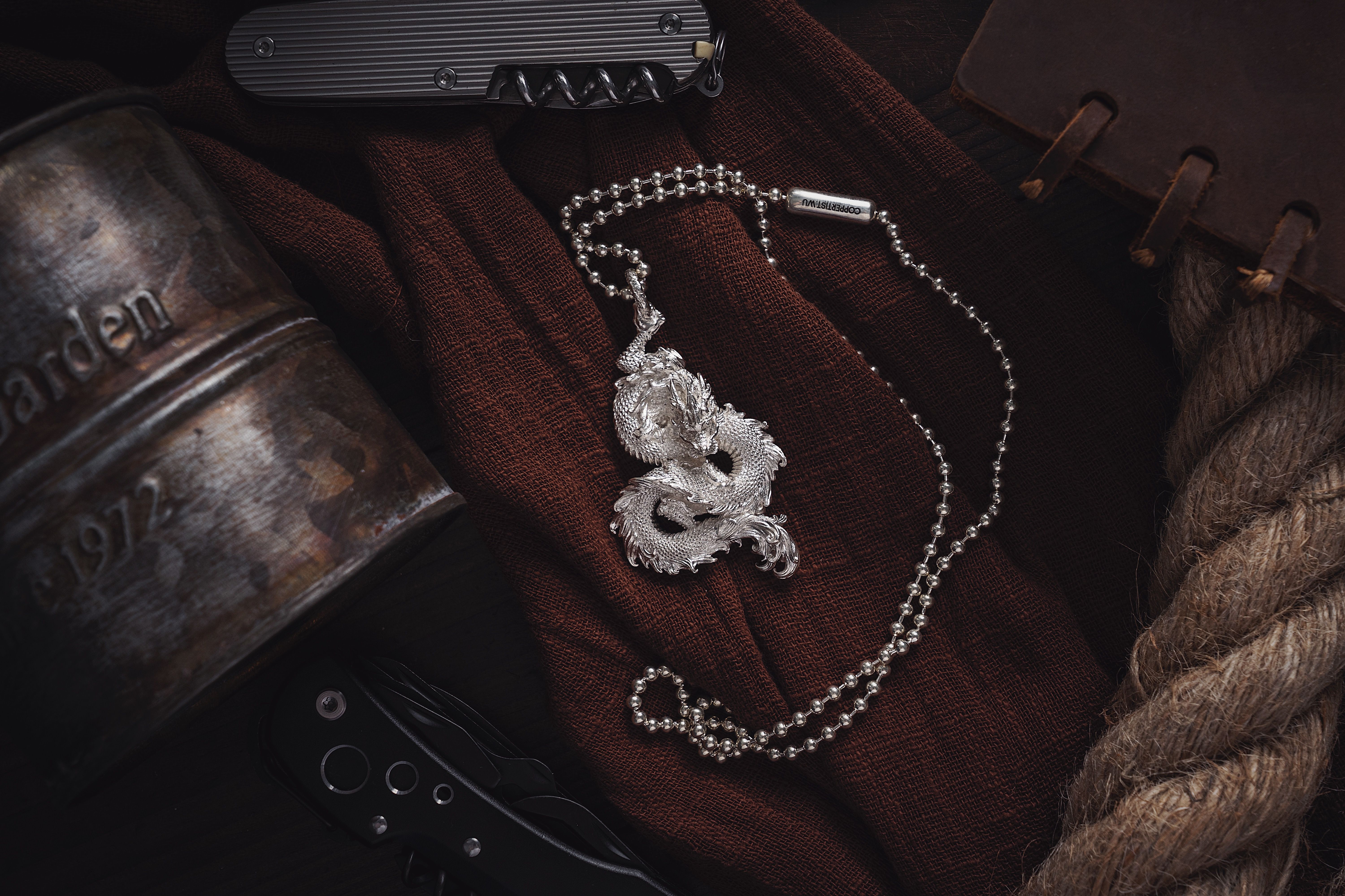 Silver dragon pendant necklace displayed on a rustic brown fabric surface with accessories.
