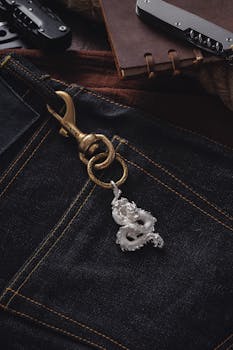Silver dragon keychain attached to dark denim jeans with a rustic and artistic backdrop.