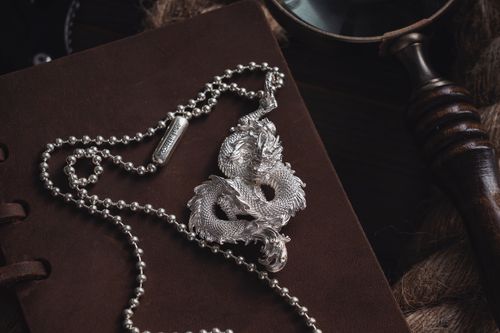 Free Elegant silver dragon pendant necklace on a dark leather surface showcasing detailed craftsmanship. Stock Photo