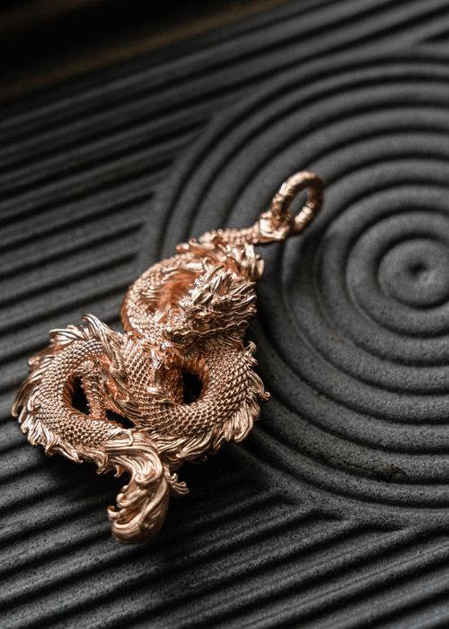 Free Elegant golden dragon pendant placed on a spiral textured background, showcasing intricate design details. Stock Photo