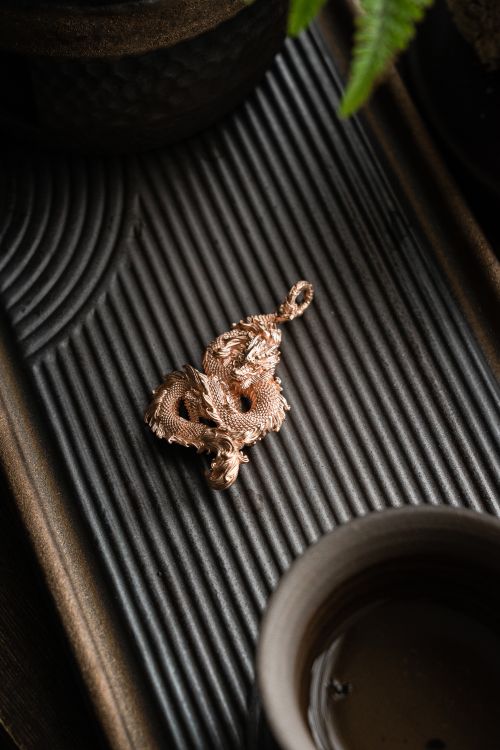 Free Close-up of a golden dragon pendant on a rippled metallic tray, showcasing intricate details and elegance. Stock Photo