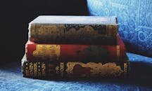 蓝色布艺沙发上堆着一摞带有装饰性装订的古董书籍