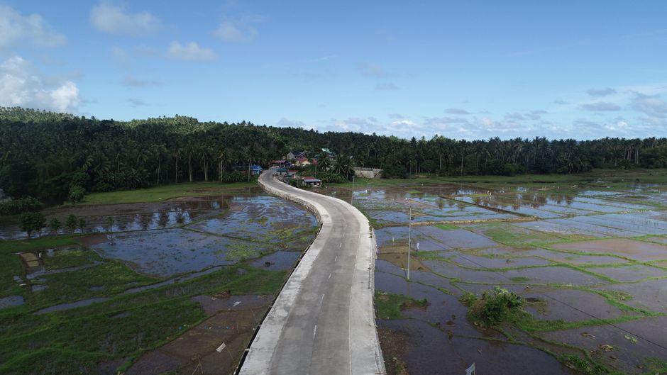 Aerial view of a winding road through lush rice paddies in Santa Magdalena, Philippines.