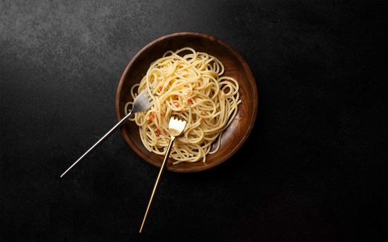 Top view of spaghetti in a wooden bowl with metallic forks on a dark background.