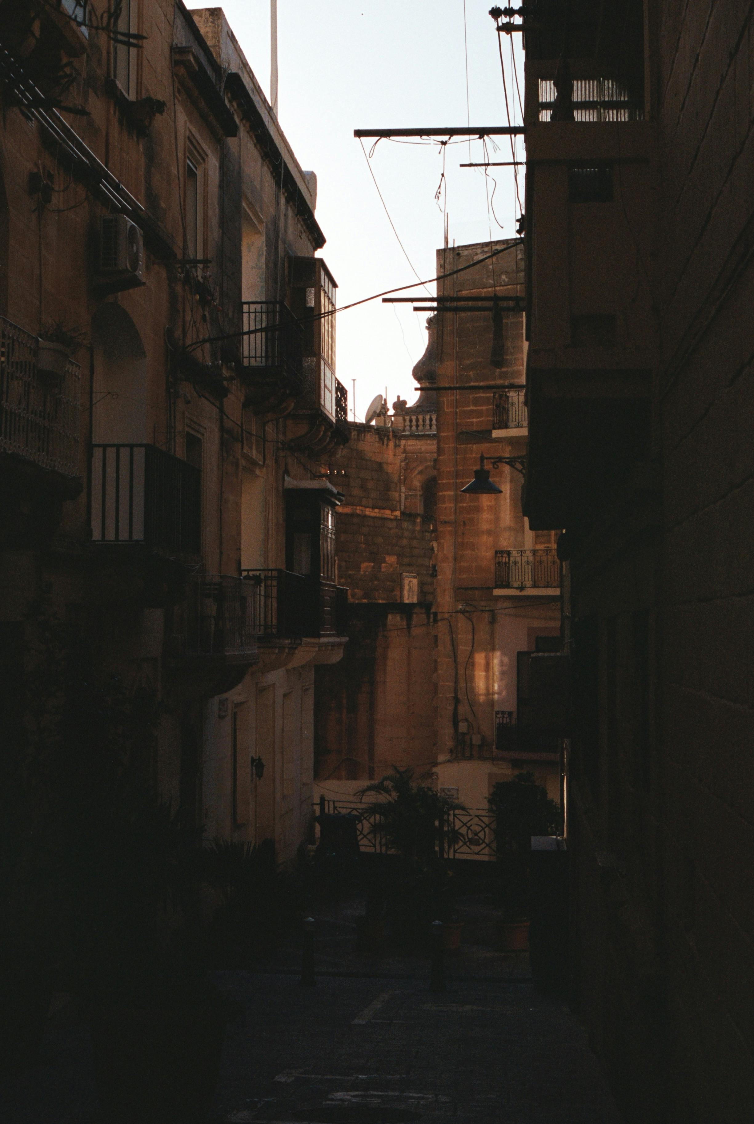 A narrow, shadowy alley in Malta revealing historic architecture under soft lighting.