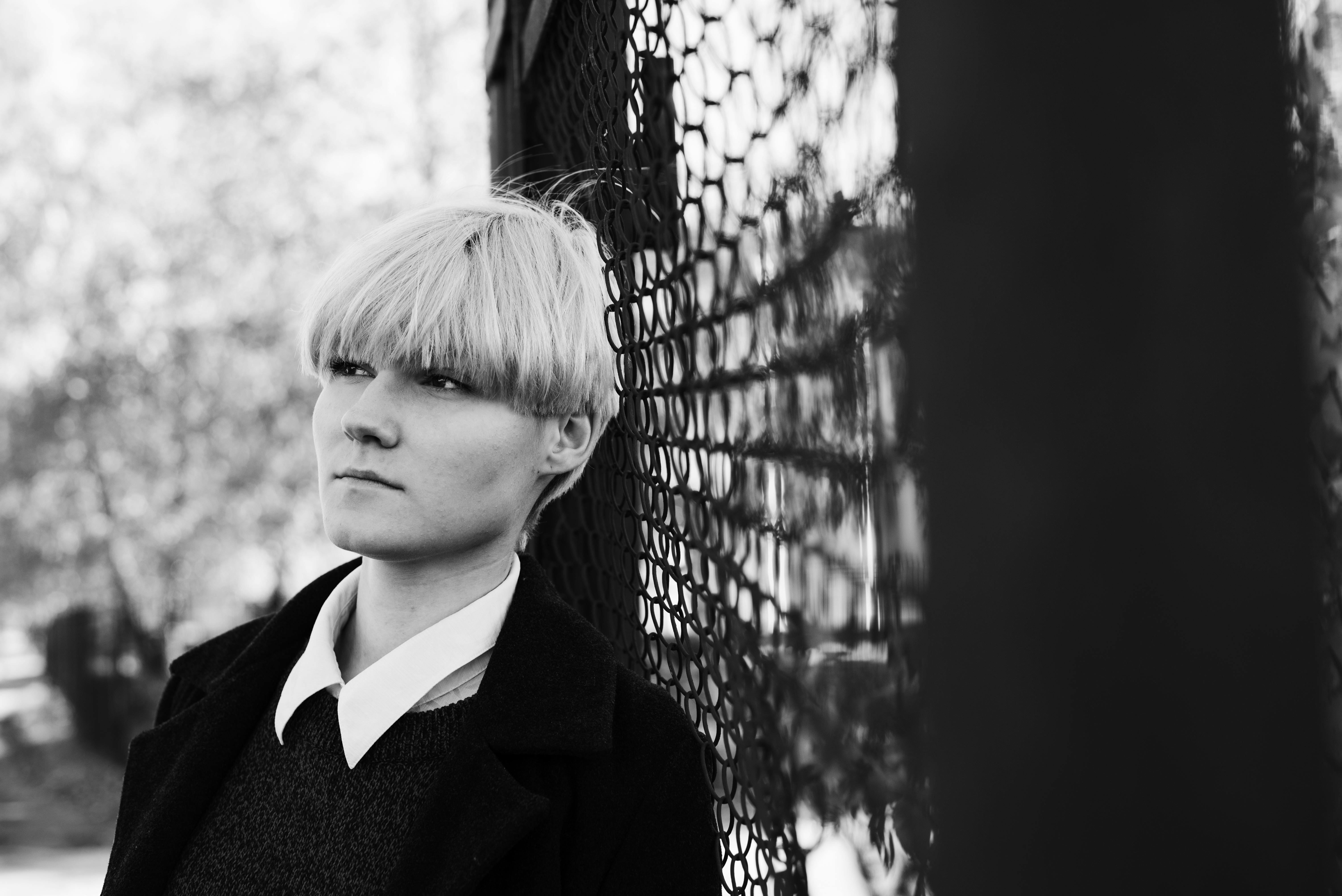 Black and white portrait of a woman leaning against a fence in Kaunas, Lithuania.