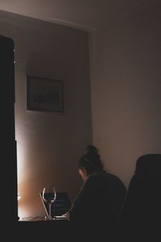 A woman works on a laptop in a dimly lit room, creating a cozy evening ambiance.