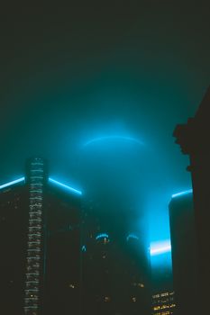 A captivating shot of illuminated skyscrapers shrouded in fog during nighttime, creating a mystical urban skyline.