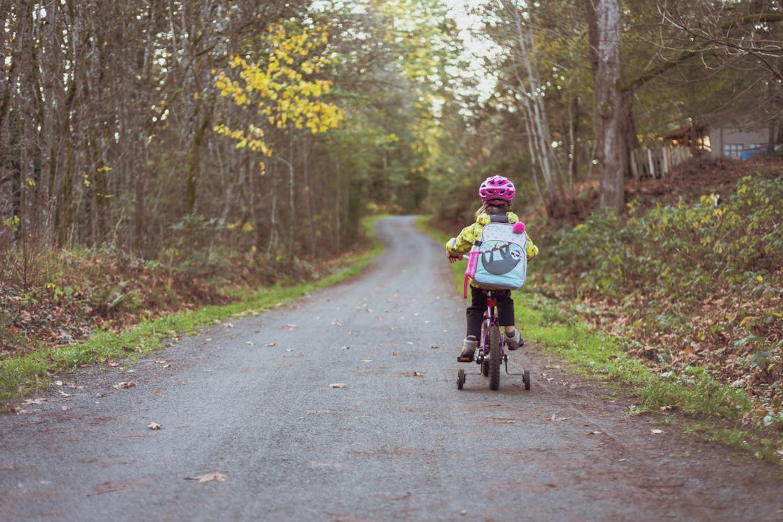 Toddler wearing a helmet and a backpack riding a bicycle on the road.