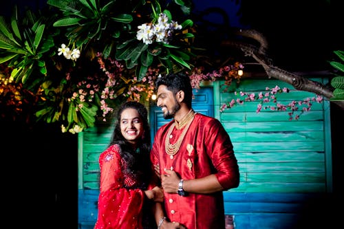 A Couple in Traditional Clothing Standing against a Blue Wall and Under a Tree