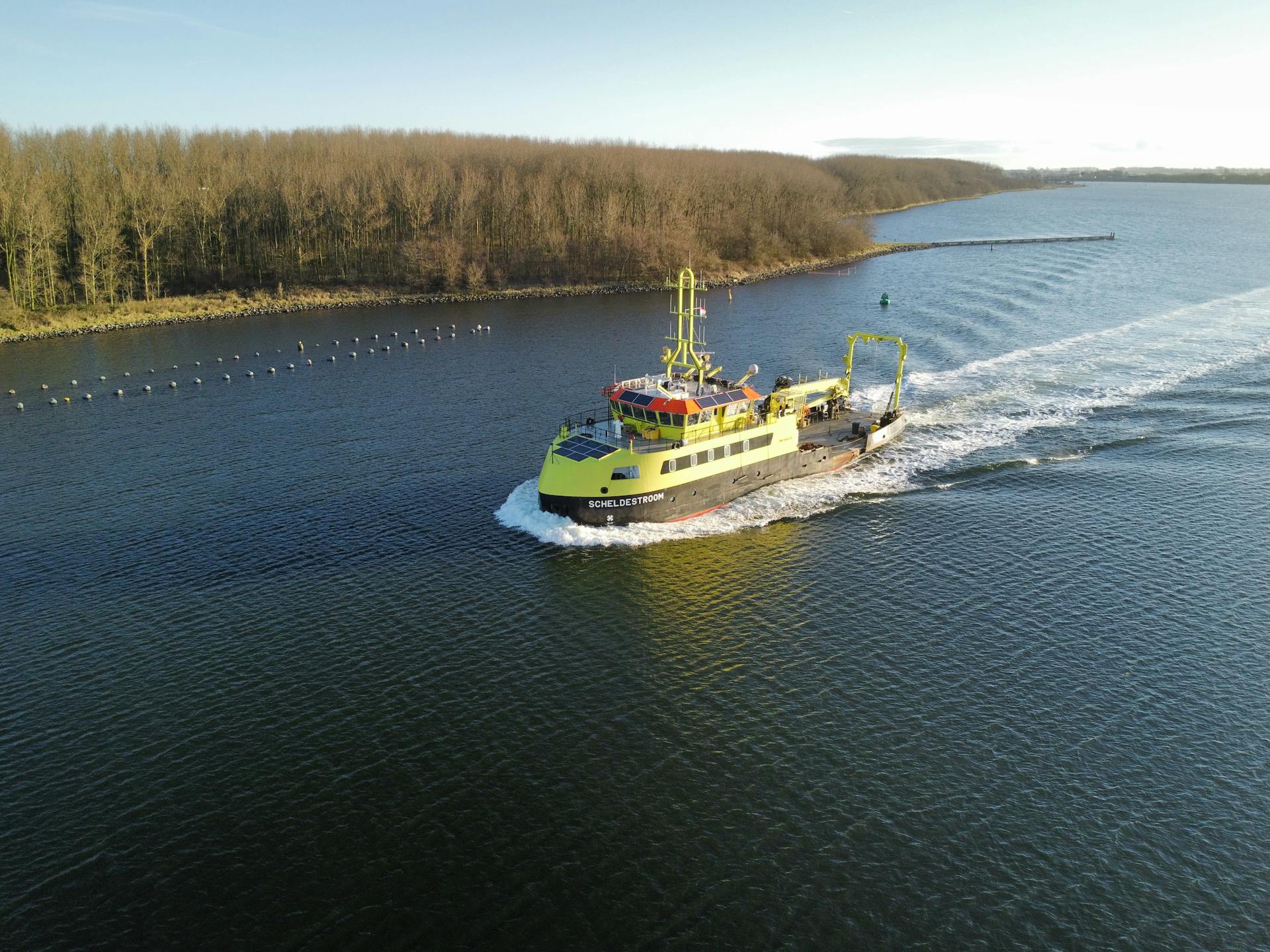 Aerial image of a research vessel sailing along a calm river surrounded by forest in autumn.