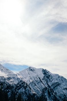Wide shot of majestic snow-covered mountain peaks against a bright, cloud-streaked sky.