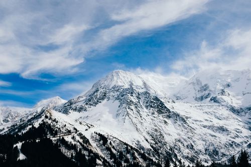 Free Stunning snow-covered peaks with dramatic white clouds under a clear blue sky. Stock Photo