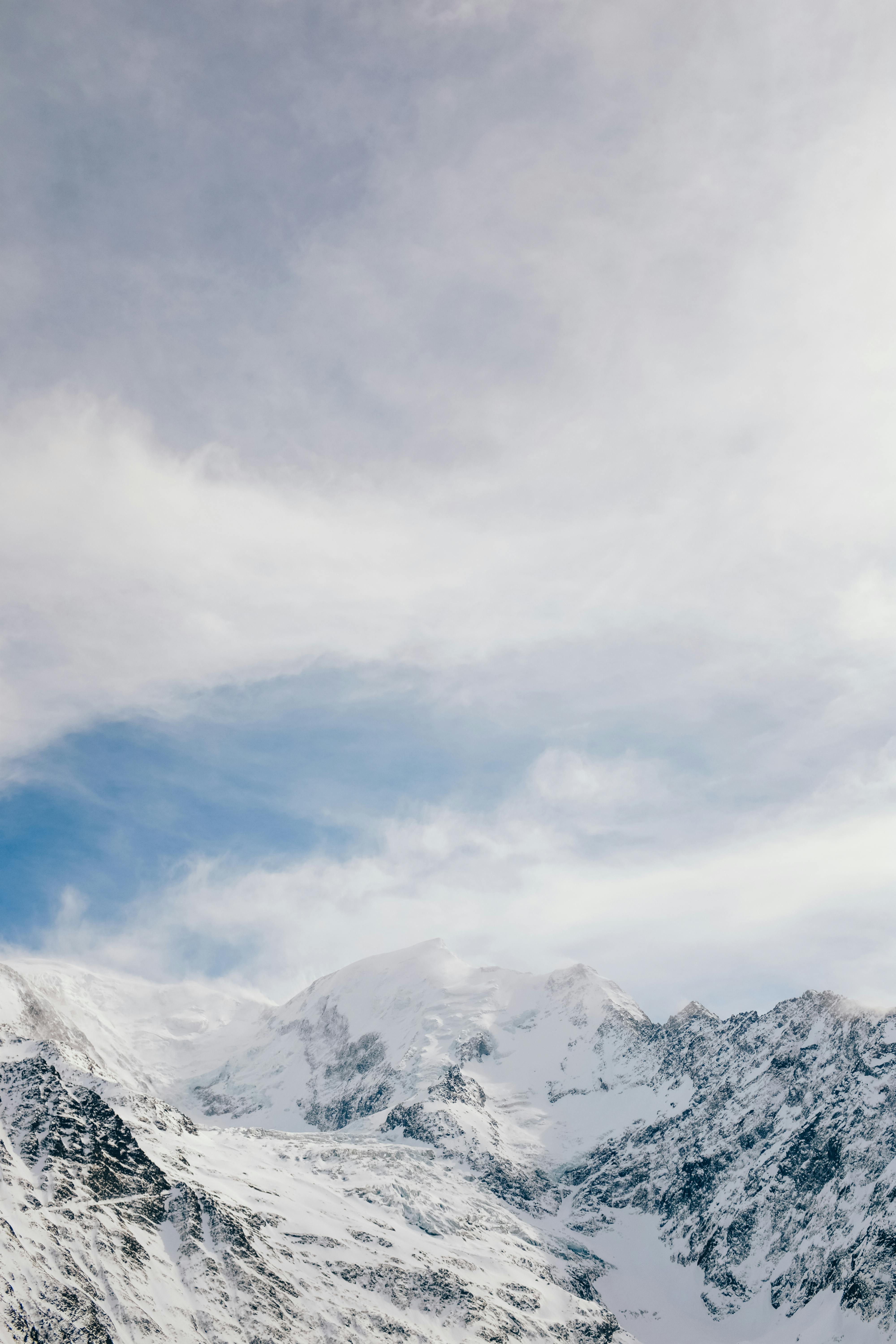 Majestic snow-covered mountains rise beneath a vast blue sky with scattered clouds.