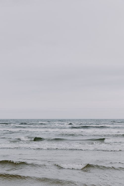 Free A serene view of an overcast sea and gentle waves on a cloudy day at the shore. Stock Photo