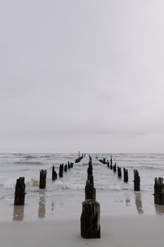 Calm sea view with old wooden posts on an overcast beach.