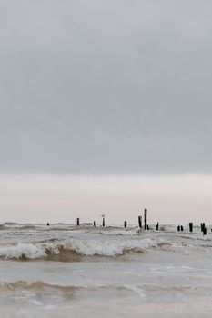 Serene coastal scene featuring gentle waves and weathered posts under a cloudy sky, reflecting a tranquil seaside ambiance.