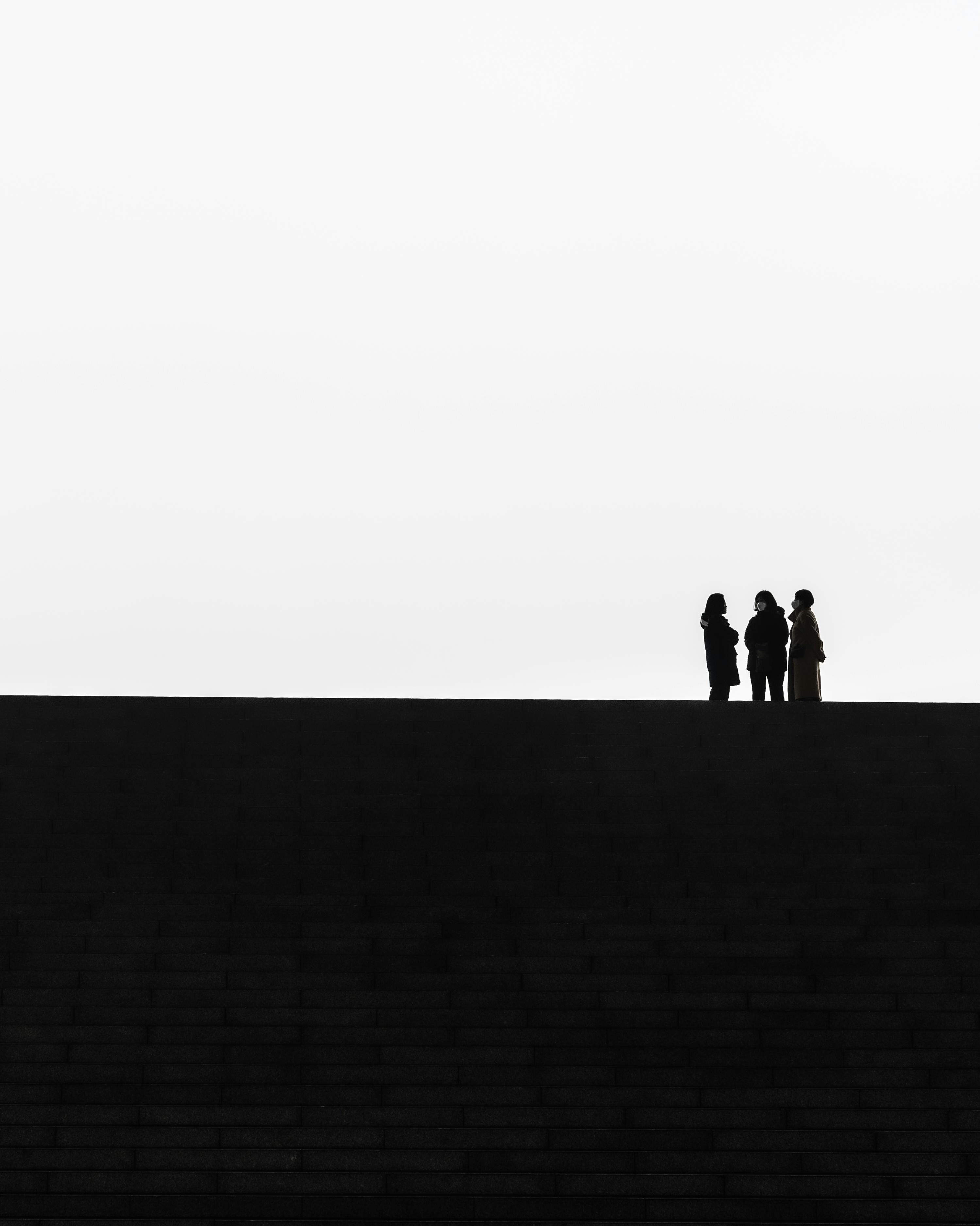 Minimalist photo capturing three silhouettes standing on city steps, emphasizing solitude.