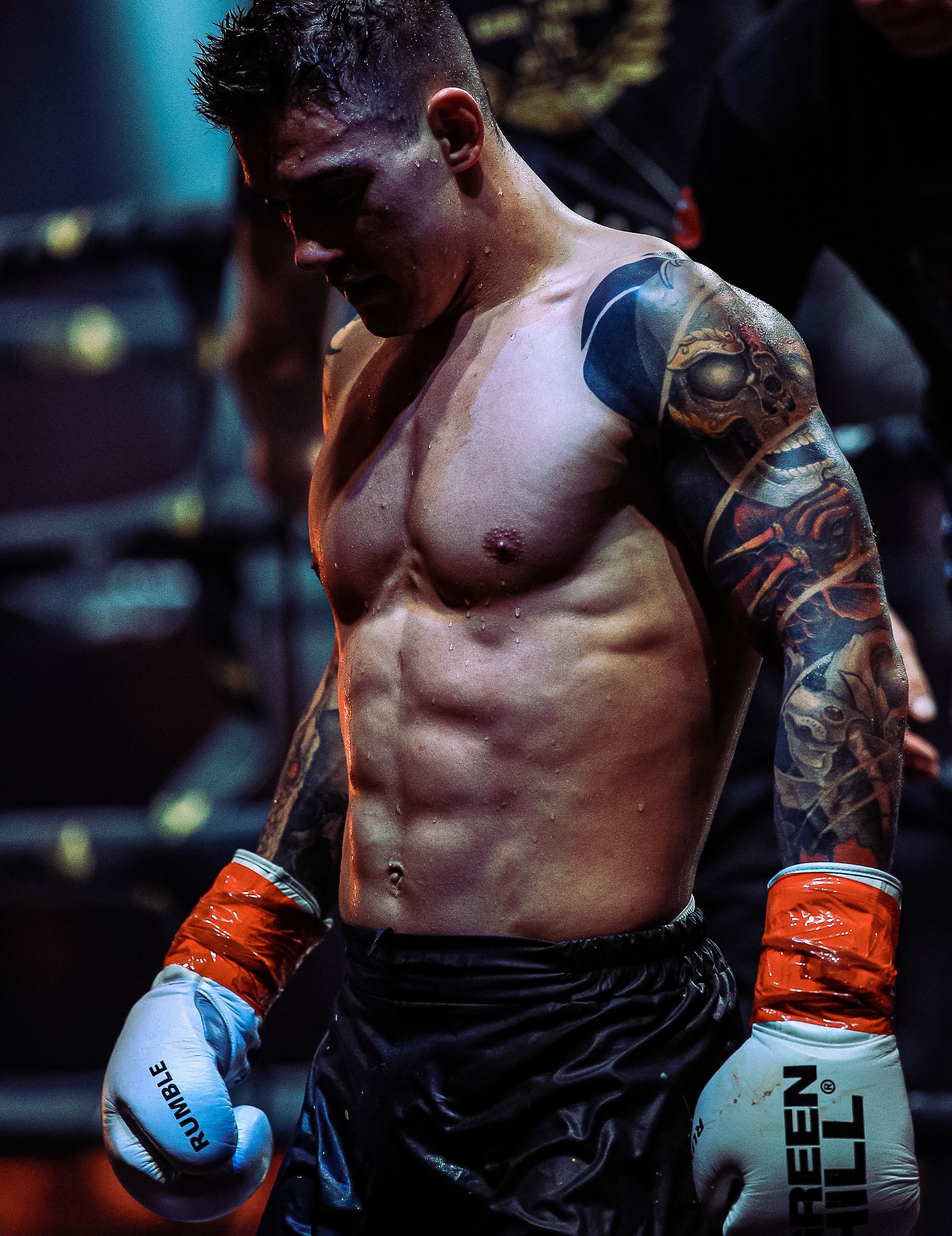 Muscular boxer with tattoos in a ring, showcasing strength and focus.
