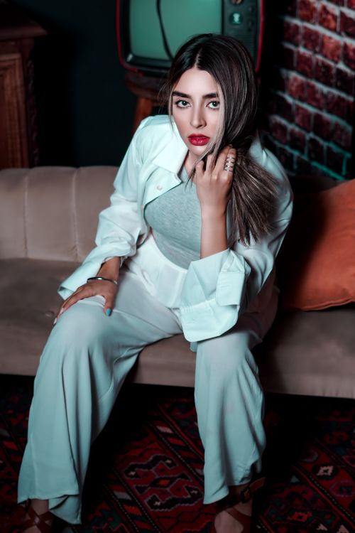 Free Stylish young woman in casual attire sitting on a sofa with striking red lips, indoors. Stock Photo