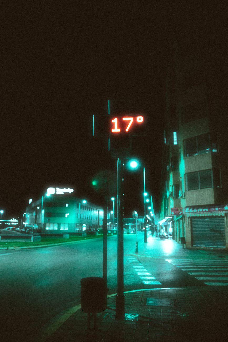 Moody urban street view in Valencia at night with prominent neon lights and a 17-degree temperature display.