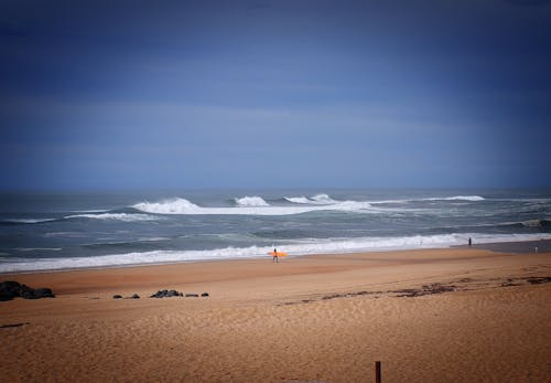 A Person with a Surfboard Walking on the Beach 