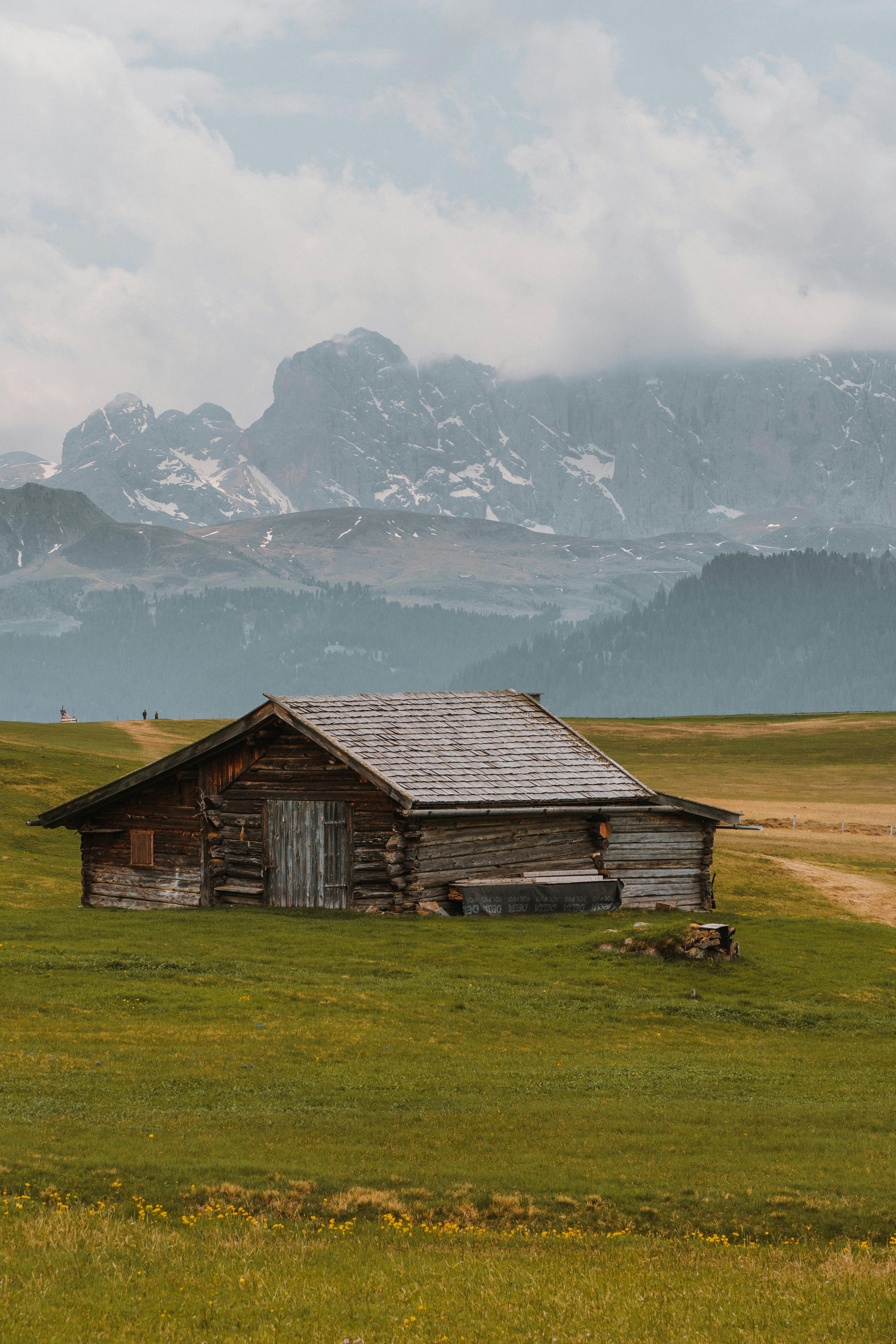 Charming wooden house set in lush fields with mountain backdrop in Trentino-Südtirol, Italy.