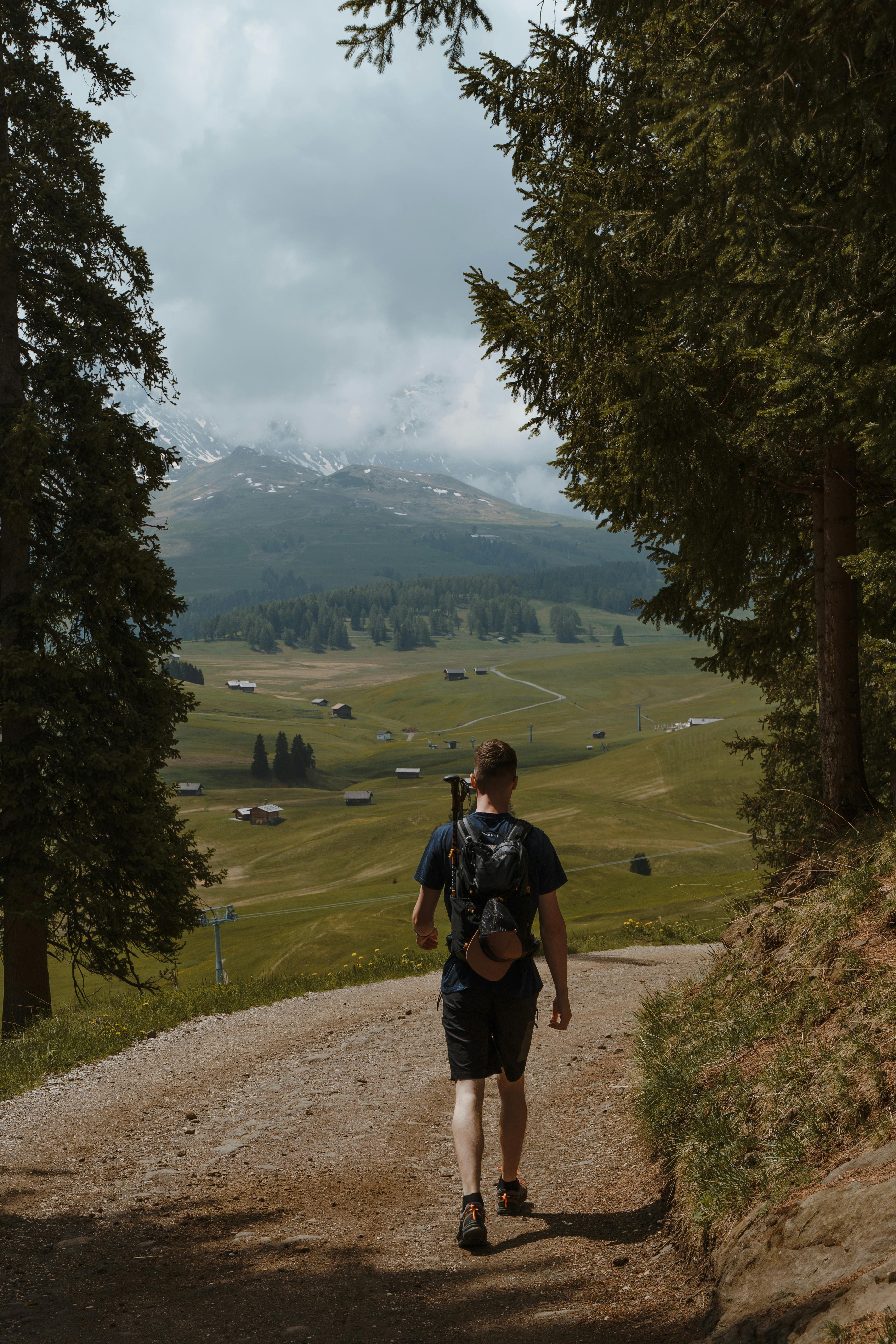 Man hiking on sunlit dirt road in Sankt Ulrich, Italy with scenic mountain landscape.