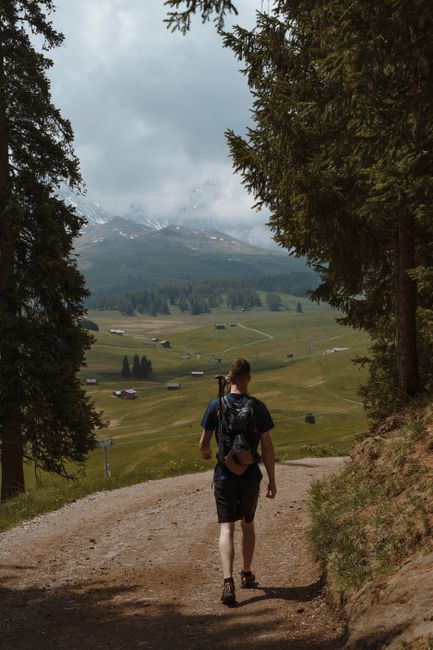 Man hiking on sunlit dirt road in Sankt Ulrich, Italy with scenic mountain landscape.