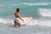 女人拿着冲浪板进入海洋，准备在阳光明媚的夏日天空下乘风破浪