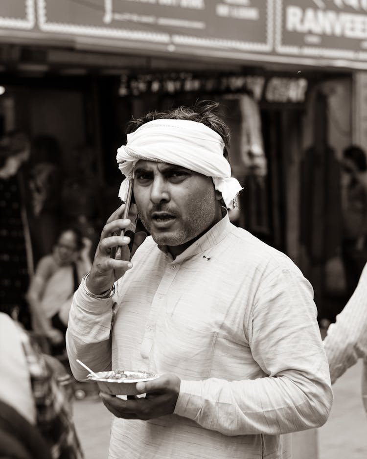 Black And White Candid Picture Of A Man Walking On The Street And Talking On The Phone 