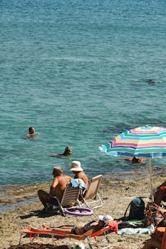 People enjoying a sunny day at a Greek beach with calm waters and a vibrant umbrella.